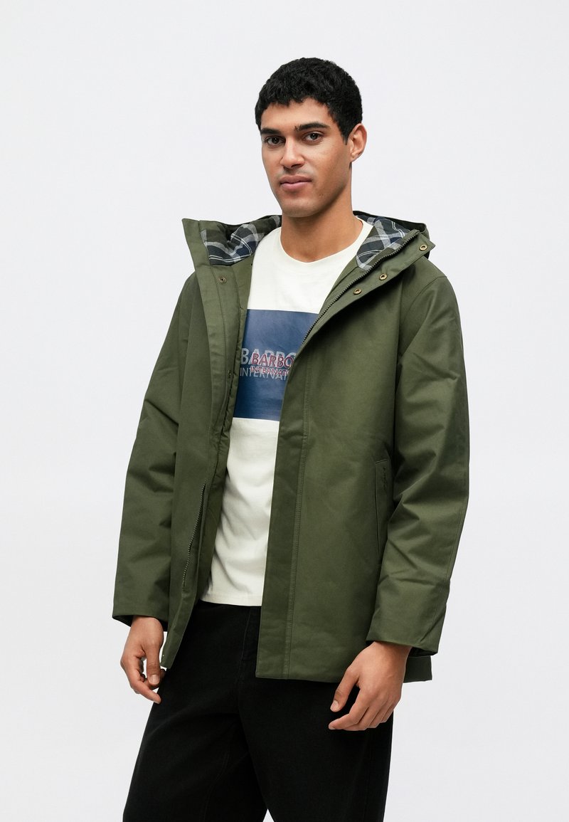 Casaco com capuz verde-oliva com fecho de correr frontal, logótipo no peito e forro às riscas. Apresenta bolsos laterais e um corte descontraído. Tecido leve.