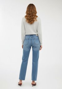 Jasnoszara swetrowa bluza, niebieskie jeansy prostego kroju z tylnymi kieszeniami oraz sandały na odsłonięte palce. Gładki materiał i luźny krój.