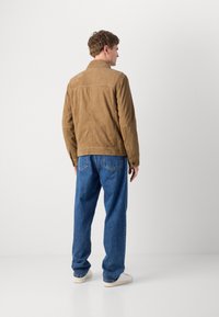 Brown suede jacket with a classic collar, featuring a textured finish. Paired with blue denim jeans and white sneakers.
