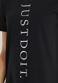 Camiseta de algodón negra con texto vertical en blanco "SÓLO HAZLO". El tejido es suave con una textura lisa, de mangas cortas y un ajuste relajado.