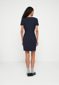 Tamsiai mėlyna trumpomis rankovėmis suknelė, aptempto silueto ir užtrauktuku nugaroje. Lygi tekstūra ir paprastas dizainas, suknelės kraštas siekia virš kelių.