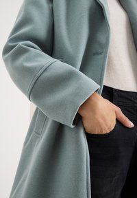 Ljusblå ullrock med en mjuk textur, en avslappnad passform och skräddarsydda ärmar, ihop med en krämfärgad tröja och svarta jeans.