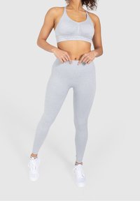 Sostén deportivo gris claro y leggings de cintura alta a juego, hechos de tela elástica, con una textura suave y un diseño ajustado.
