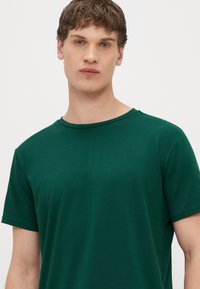 Πράσινο κοντομάνικο μπλουζάκι από μαλακό ύφασμα, με στρογγυλή λαιμόκοψη και ομαλή, ομοιόμορφη υφή χωρίς ορατά σχέδια ή διακοσμητικά στοιχεία.