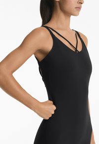 Zwarte mouwloze body met kruisbanden, gladde textuur, slim fit ontwerp en zijpaneel details, die een silhouet vanuit een lichte hoek toont.