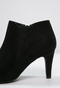 Stivali neri in camoscio alla caviglia con forma affusolata, pannelli laterali elastici e tacco a stiletto di 5 cm. Texture liscia, design minimalista.