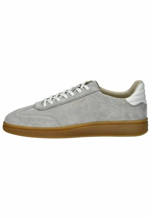 Zapatilla de ante gris con acento blanco en el talón, cordones de un tono blanco roto y suela de goma. Presenta una puntera redondeada y un branding mínimo.