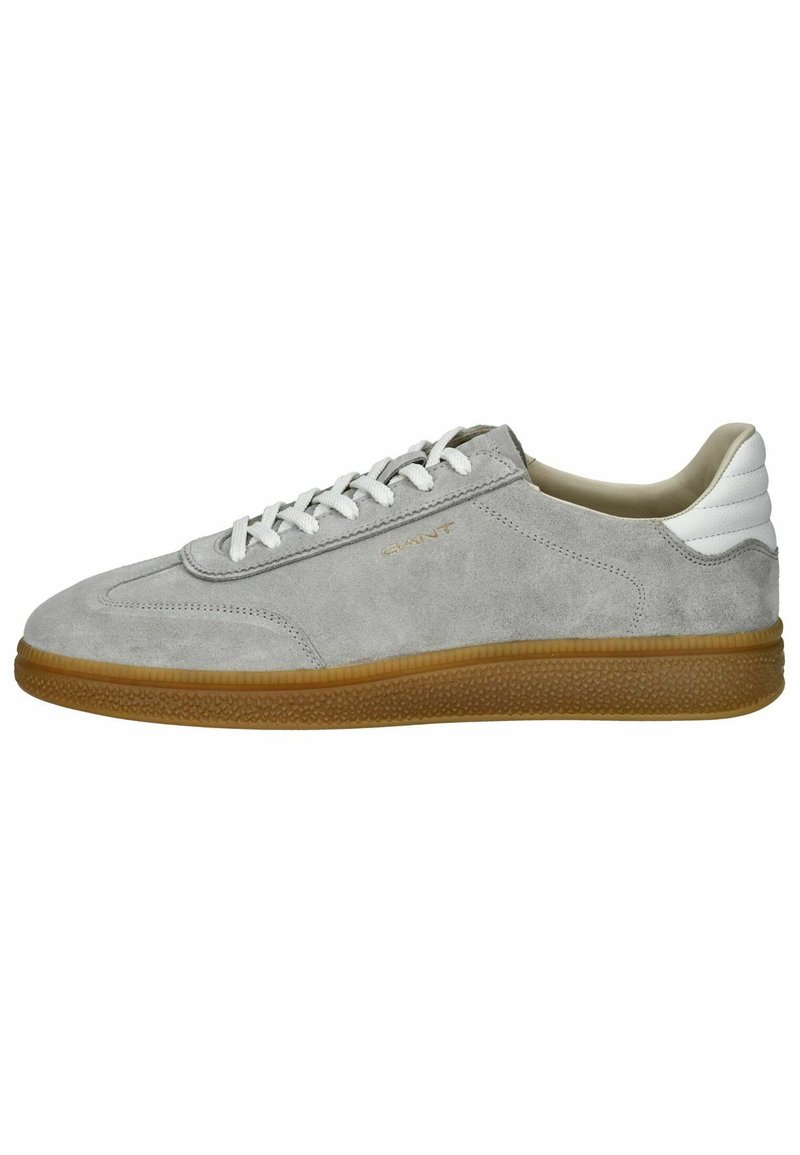 Zapatilla de ante gris con acento blanco en el talón, cordones de un tono blanco roto y suela de goma. Presenta una puntera redondeada y un branding mínimo.