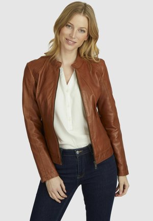 Veste en cuir marron avec un col rond, fermeture éclair à l'avant et design ajusté, portée sur un chemisier blanc et un jean foncé. Texture lisse.