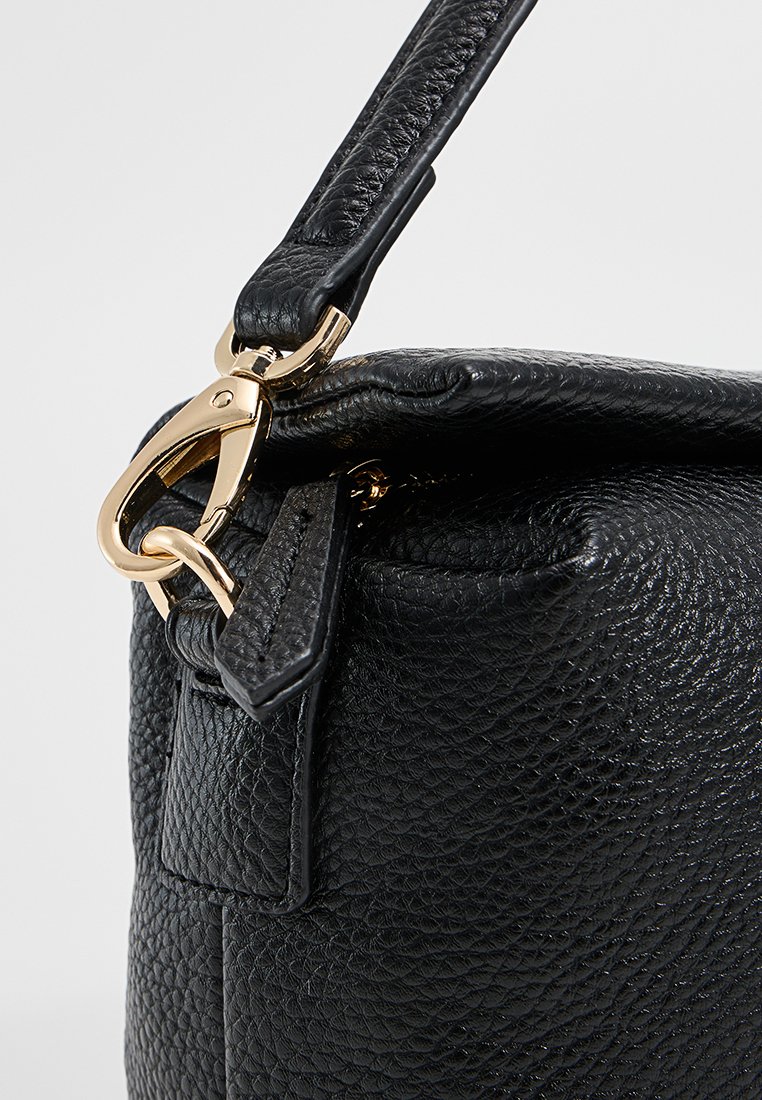 Sac en cuir texturé noir avec un fermoir et une bandoulière en matériel doré. Le sac présente une forme structurée et une doublure intérieure lisse.