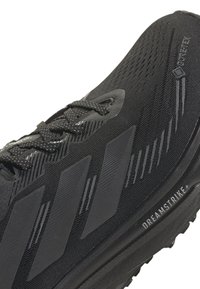 Scarpa atletica nera con tre strisce scure, lacci neri, tomaia in Gore-Tex e testo "DREAMSTRIKE+" sulla suola.