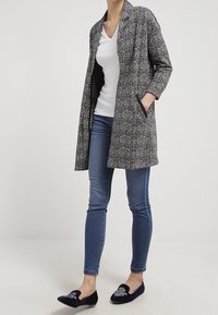 Svart och vitmönstrad kappa med långa ärmar, öppen front och sidofickor, parat med blå skinny jeans och marinblå ballerinas.