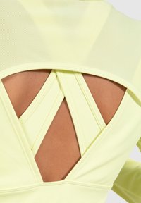 Gelbe Sportbekleidung mit einem Netzrücken verfügt über gekreuzte Träger, die Haut zeigen. Glatte Textur mit verstärkten Nähten.