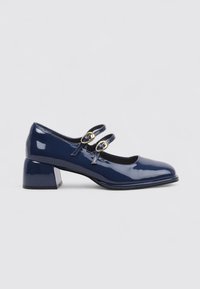 Zapato Mary Jane de charol azul marino con tacón cuadrado y dos correas ajustables en el lateral, exhibido sobre un fondo blanco.