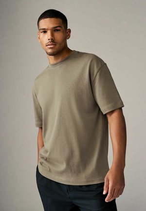 Oliven grøn bomulds t-shirt med korte ærmer, rund hals, afslappet pasform og glat tekstur. Sammen med sorte bukser.