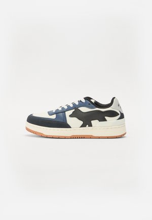 Low-top sneaker in white, navy, and black leather. Features a prominent fox silhouette on the side and a textured gum rubber sole.