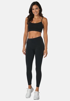Sort sportsbh med tynde stropper parret med højtaljede sorte leggings. Begge beklædningsgenstande har et glat, strækbart stof og en tætsiddende design.
