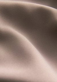 Tejido marrón claro con una sutil textura acanalada, que presenta suaves y lisas olas y delicados pliegues en la superficie.
