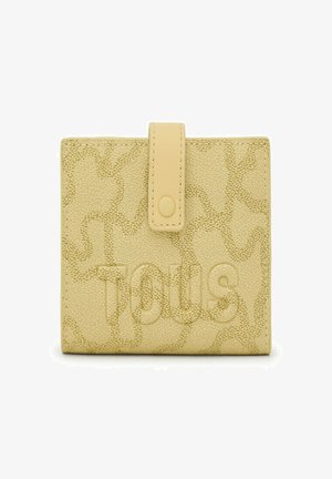 Billetera amarilla texturizada con cierre de solapa y botón. Presenta un sutil patrón estampado y el nombre de la marca "Tous" mostrado de manera prominente.