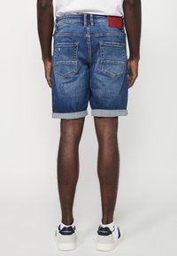 Jeans kratke hlače s srednje modrim pranjem, zloženi robovi in dvema zadnjima žepoma. Imajo usnjen znak na hrbtni pasu.