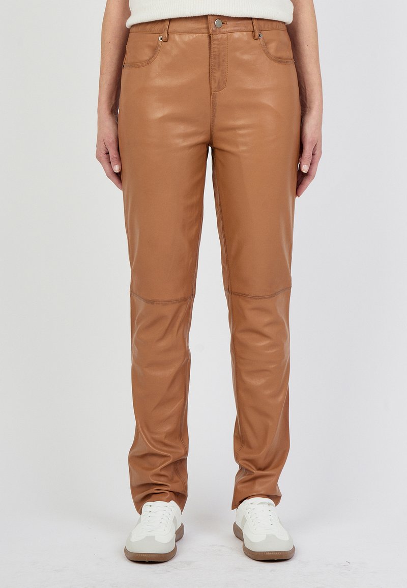 Bruine leren broeken met een gladde textuur, met een slim fit ontwerp, voorzakken en gedetailleerde stiksels op de knieën. Gepaard met witte sneakers.