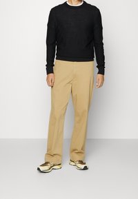 Maglione nero a maglia, pantaloni beige a gamba larga e sneakers con dettagli gialli. Design semplice con polsini a coste e scollatura rotonda.