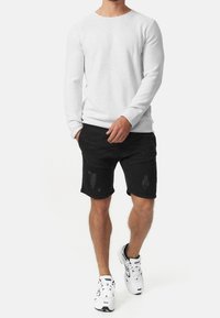 Valkoinen pitkähiha-pusero, jossa poikkileikattu neulos, yhdistetty mustiin kuluneisiin shortseihin, joissa vaakasuorat viivat ja taskut. Valkoiset lenkkarit.