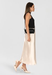 Top negro sin mangas con ribetes, falda midi de satén color crema, tacones altos beige con recortes y un pequeño bolso de hombro negro con detalle de texto.