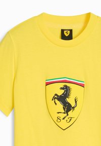 Ljusa gula t-shirt med den ikoniska svarta, prancing horse-logotypen inom en sköld, accentuerad av en tri-färgstripe ovanför.
