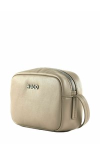 Beige Ledertasche mit strukturierter Oberfläche, Reißverschluss und seitlichem Griff. Auf der Vorderseite prangt die silberne "HUGO"-Marke. Kompakte rechteckige Form.