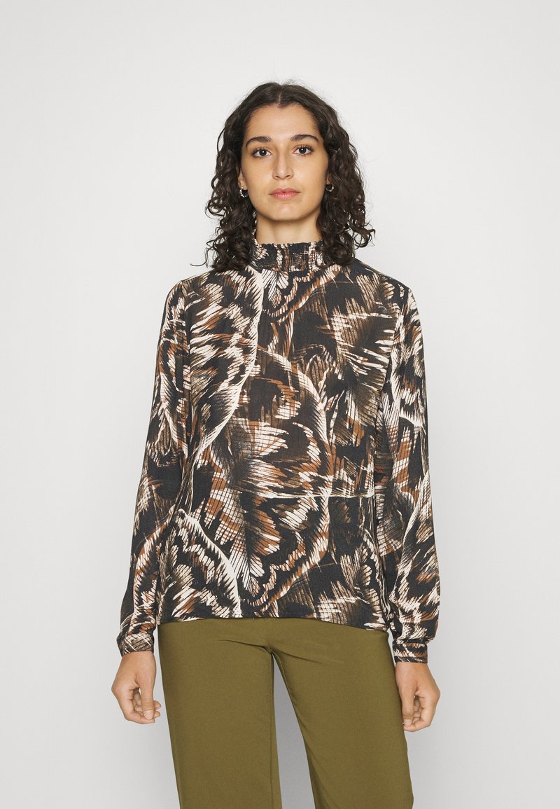 Blusa de mangas longas com um decote alto, apresentando um padrão abstrato em tons de castanho, preto e branco em tecido suave. Combinada com calças verde-oliva.