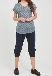 Blusa blu con motivo, maniche corte e scollatura a V, abbinata a pantaloni cropped blu scuro con polsini elastici e mocassini neri.