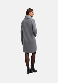 Abito lavorato a maglia grigio con colletto alto, maniche lunghe e vestibilità comoda, abbinato a stivaletti neri alla caviglia e collant trasparenti. Dettagli in tessuto testurizzato.