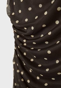 Czarna przezroczysta tkanina w białe kropki, marszczona i zebrana, tworząca teksturowane fałdy i drapowanie.