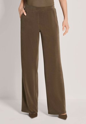 Locker sitzende braune Hose mit Seitentaschen, getragen von einer stehenden Person, kombiniert mit passenden spitzen Schuhen.