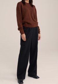 Pull en mohair marron avec un col rond, associé à un pantalon cargo large noir avec poches latérales et bottes à talons noires plates.