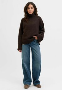 Brązowy sweter z golfem o dzianinowym wykończeniu, z prążkowanymi mankietami, zestawiony z luźnymi, wysokim stanem niebieskimi dżinsami oraz brązowymi butami typu slip-on.