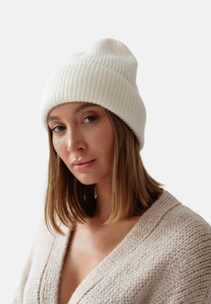 Biała, prążkowana czapka beanie o miękkiej fakturze, z zawiniętym mankietem. Noszona w sposób casualowy, uzupełniona neutralnym kardiganem.