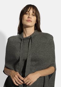 Capa de mezcla de lana gris con un cuello alto y lazos en el frente. Presenta un acabado texturizado y aberturas para los brazos para mayor comodidad al usarla.