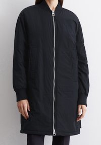 Czarna bomberka o gładkiej teksturze, z prążkowanymi mankietami, zamek błyskawiczny, dwie przednie kieszenie oraz kieszeń na ramieniu.