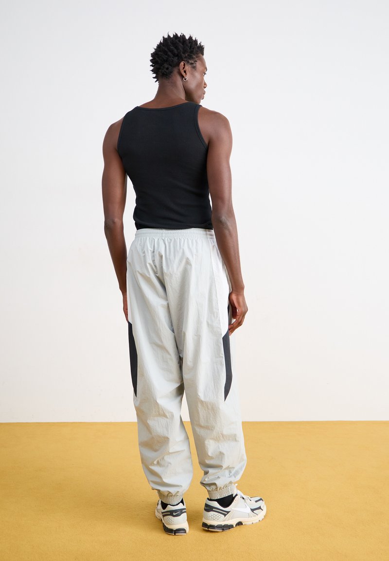 Débardeur noir sans manches et joggers gris clair avec des empiècements latéraux noirs. Les joggers possèdent une taille élastique et des ourlets à bord-coupé. Baskets noir et blanc.