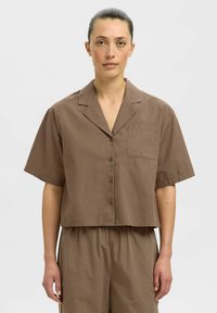 Braunes kurzärmliges Cropped-Shirt aus einem leichten Stoff, mit spitzem Kragen, vorderer Knopfverschluss und einer Brusttasche.