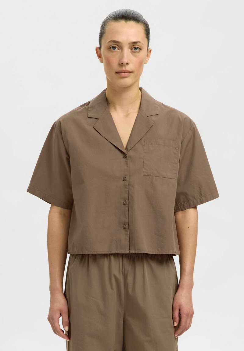 Braunes kurzärmliges Cropped-Shirt aus einem leichten Stoff, mit spitzem Kragen, vorderer Knopfverschluss und einer Brusttasche.