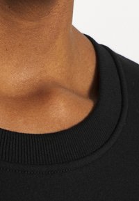 Czarny sweter z okrągłym żebrowanym dekoltem, gładka tekstura oraz zbliżenie na kołnierz. Miękka tkanina z subtelnym połyskiem.