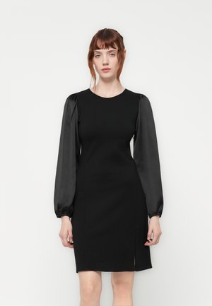 Black dress with fitted bodice, round neckline, and black satin puff sleeves. Features a knee-length hem with a side slit for mobility.