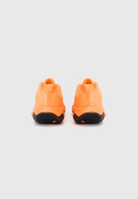 Chaussures de sport oranges avec une semelle extérieure noire texturée et une tige lisse. Pas de marquage visible. La vue arrière montre la construction du talon.