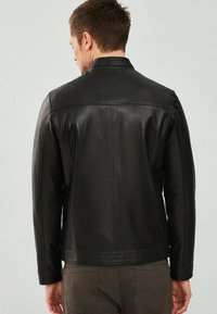 Zwart leren jasje met een slim fit, voorzien van een klassieke kraag, een gladde textuur en nette stiksels op de rug en schouders.