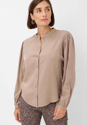 Blusa beige a maniche lunghe con colletto a fascia, chiusura frontale a bottoni e maniche arricciate. Tessuto morbido e scivoloso. Abbinata a pantaloni con stampa animale.