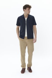 Chemise bleu marine à manches courtes avec un design à boutons, associée à un chino beige et des chaussures à lacets marron foncé. Silhouette simple et moderne.