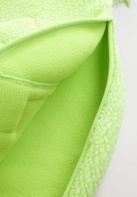 Jasnozielony materiał polarowy z miękką, teksturalną warstwą zewnętrzną i gładką, pluszową warstwą wewnętrzną, złożony, aby pokazać obie tekstury.